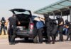 customs officers detain a person beside a car with its trunk open