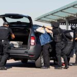ICE Shot Sparks Austin Street Fury customs officers detain a person beside a car with its trunk open