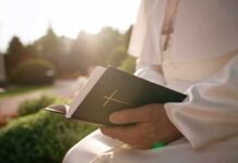 Person in white robe holding a Bible outdoors