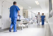 A Veteran Comedian Remains Under Hospital Care Susan Fuhrmann walking with a nurse in a bright hospital corridor