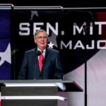 Man in suit speaking at a podium on a stage
