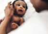 Baby lying on a bed looking up at an adult