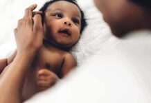 Baby lying on a bed looking up at an adult