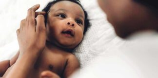 Baby lying on a bed looking up at an adult