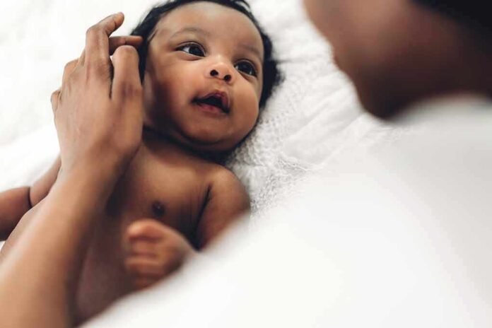 Baby lying on a bed looking up at an adult