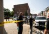 Police officers secure an urban street with yellow tape near patrol cars