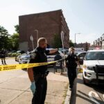 Police officers secure an urban street with yellow tape near patrol cars
