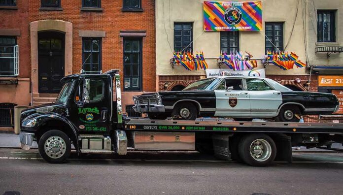shutterstock_1960240633 Tow truck carrying vintage sheriff car on city street
