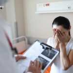 Woman covering her face while doctor holds a clipboard in a hospital room