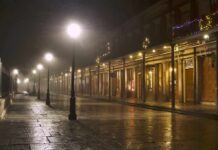 Foggy street with lit lampposts and decorated storefronts at night