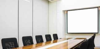 Conference room with long wooden table and empty chairs facing a blank projection screen