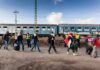 Group of people walking past a blue passenger train with police nearby
