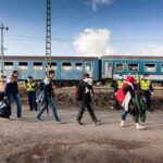 Group of people walking past a blue passenger train with police nearby