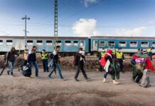Group of people walking past a blue passenger train with police nearby