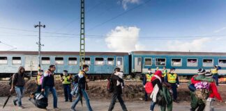 Group of people walking past a blue passenger train with police nearby
