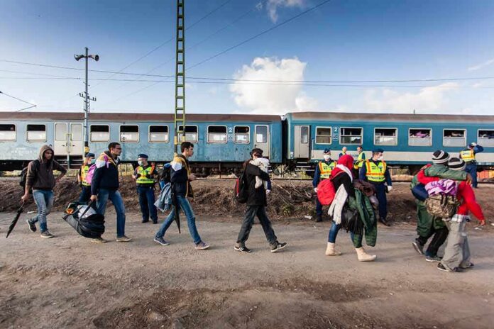 Group of people walking past a blue passenger train with police nearby
