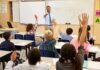 Teacher at front of classroom as students raise hands