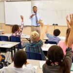 School Face Ban Explodes Into Culture War Teacher at front of classroom as students raise hands