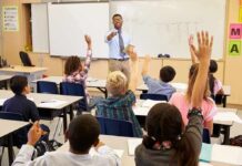 Teacher at front of classroom as students raise hands