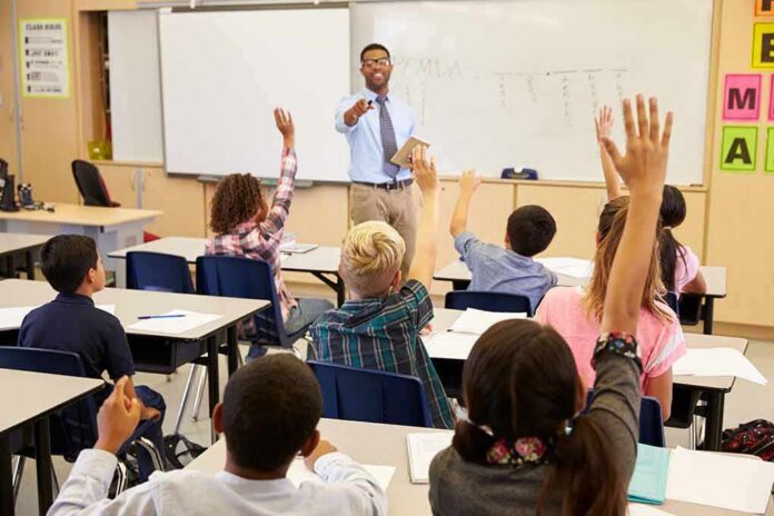 Teacher at front of classroom as students raise hands