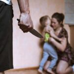 Man holding knife as woman shields child in kitchen