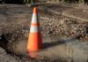 Traffic cone in a water-filled pothole on a damaged road