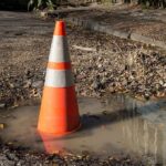 Traffic cone in a water-filled pothole on a damaged road