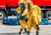 50,000 Evacuated – Now the Real Fight Begins Hazmat workers in yellow suits carry equipment near a tanker truck
