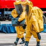 50,000 Evacuated – Now the Real Fight Begins Hazmat workers in yellow suits carry equipment near a tanker truck