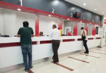Banking Regulator Uncovers Widespread Restrictions People at numbered service counters in a modern lobby