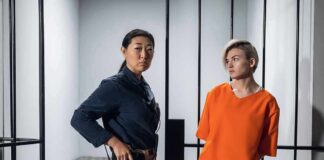 Police officer stands beside inmate in orange uniform inside a jail cell