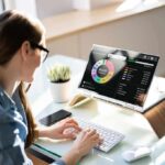 Woman working at desk with laptop showing finance dashboard