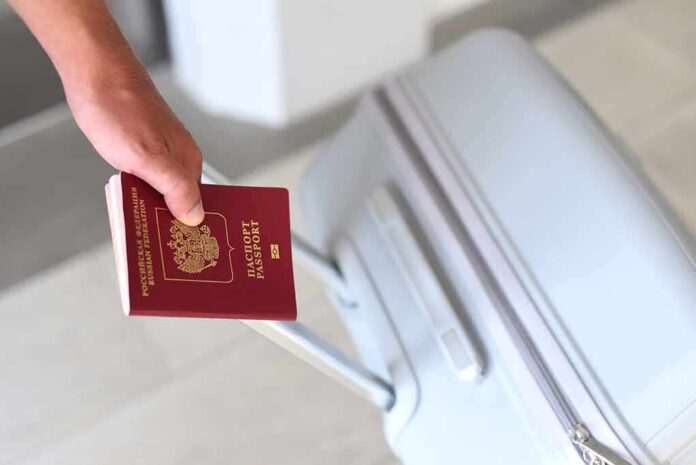 Hand holding a red passport next to a gray suitcase